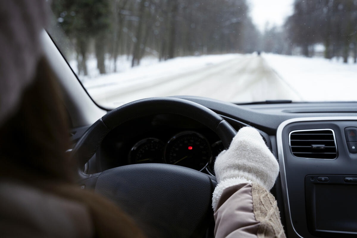 A girl driving in winter wearing clothes that are not ideal for this purpose.